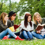 Four women reading books on a grassy field