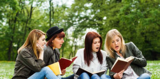 Four women reading books on a grassy field