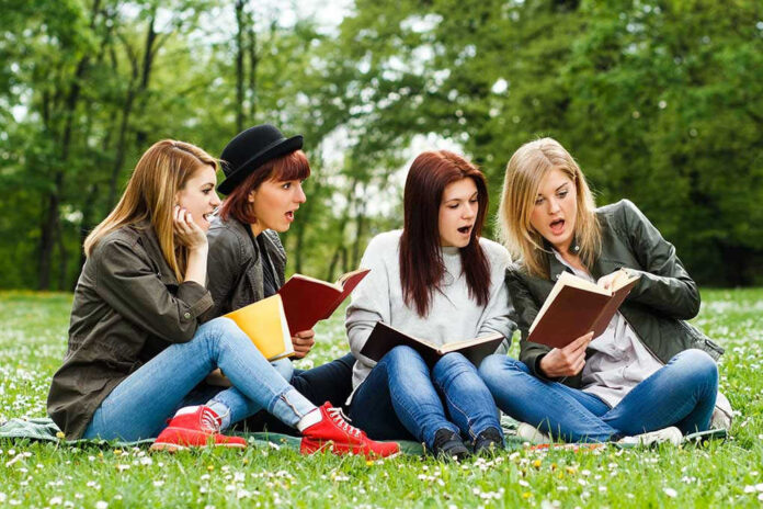 Four women reading books on a grassy field