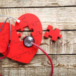 Red heart puzzle with stethoscope on wooden background