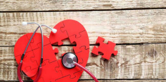 Red heart puzzle with stethoscope on wooden background