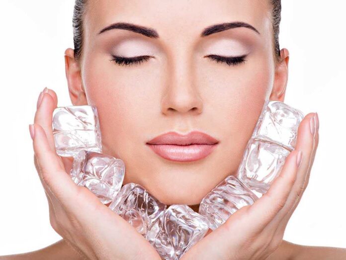 A woman with closed eyes holding ice cubes against her face
