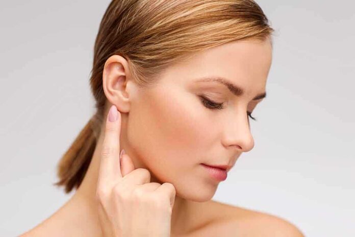 Profile view of a woman gently touching her ear with a thoughtful expression