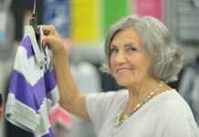 Senior woman smiling while holding a purple and gray shirt in a clothing store