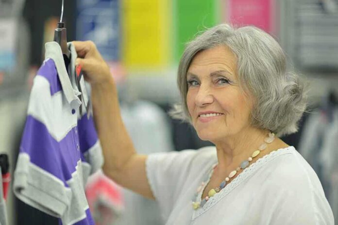 shutterstock_215551678.jpg Senior woman smiling while holding a purple and gray shirt in a clothing store