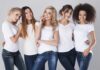 Five women in white tshirts and jeans smiling together