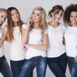 Five women in white tshirts and jeans smiling together
